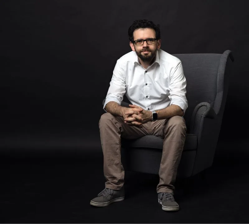 Business Coach Gerd Beidernikl sitzt auf einem grauen Sessel vor dunklem Hintergrund