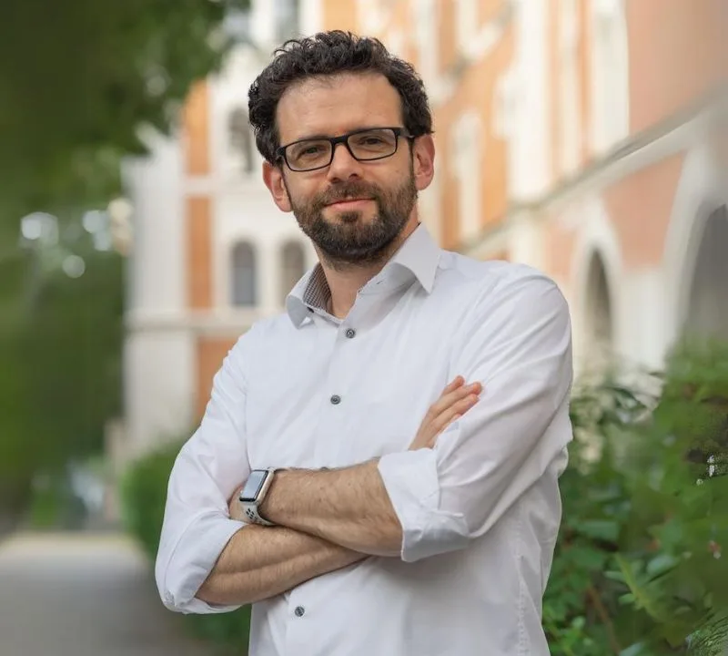 Gerd Beidernikl mit verschränkten Armen im weißen Hemd vor einem Gebäude.